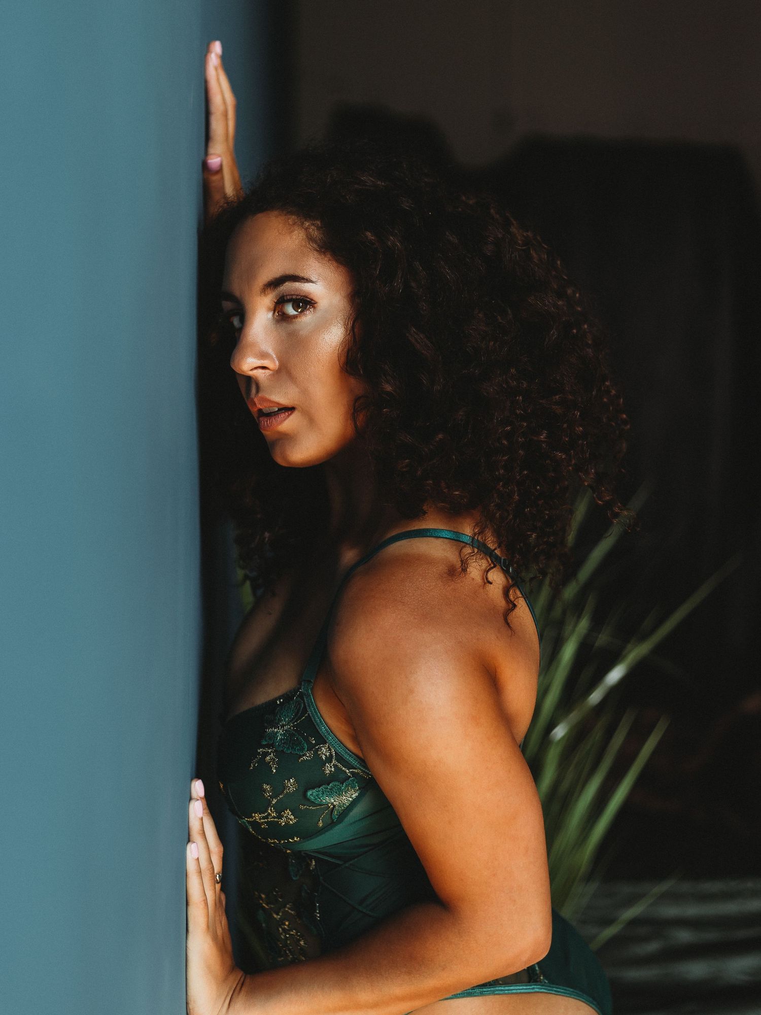 Fashion portrait in teal lingerie against blue wall with tropical plants.