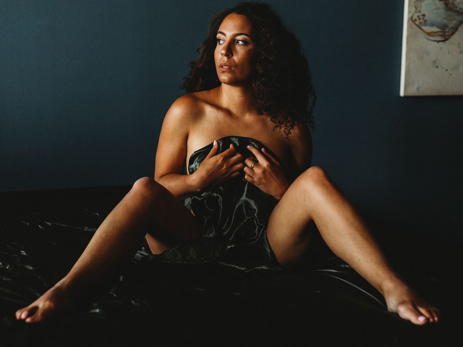 Dramatic boudoir photo on dark velvet with moody lighting.