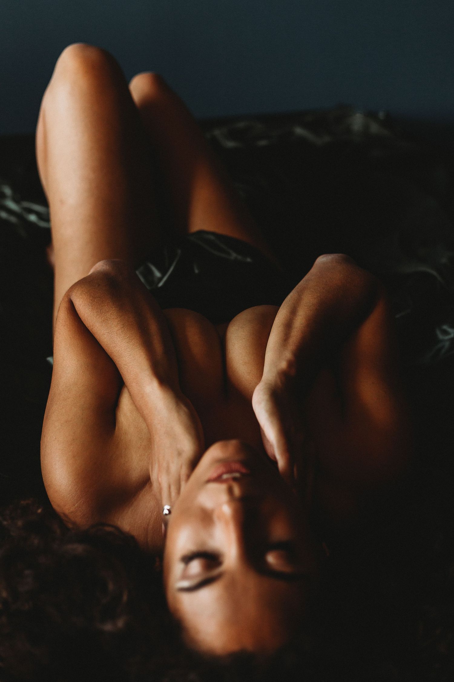 Artistic portrait of model with curly hair in moody lighting and dark background.