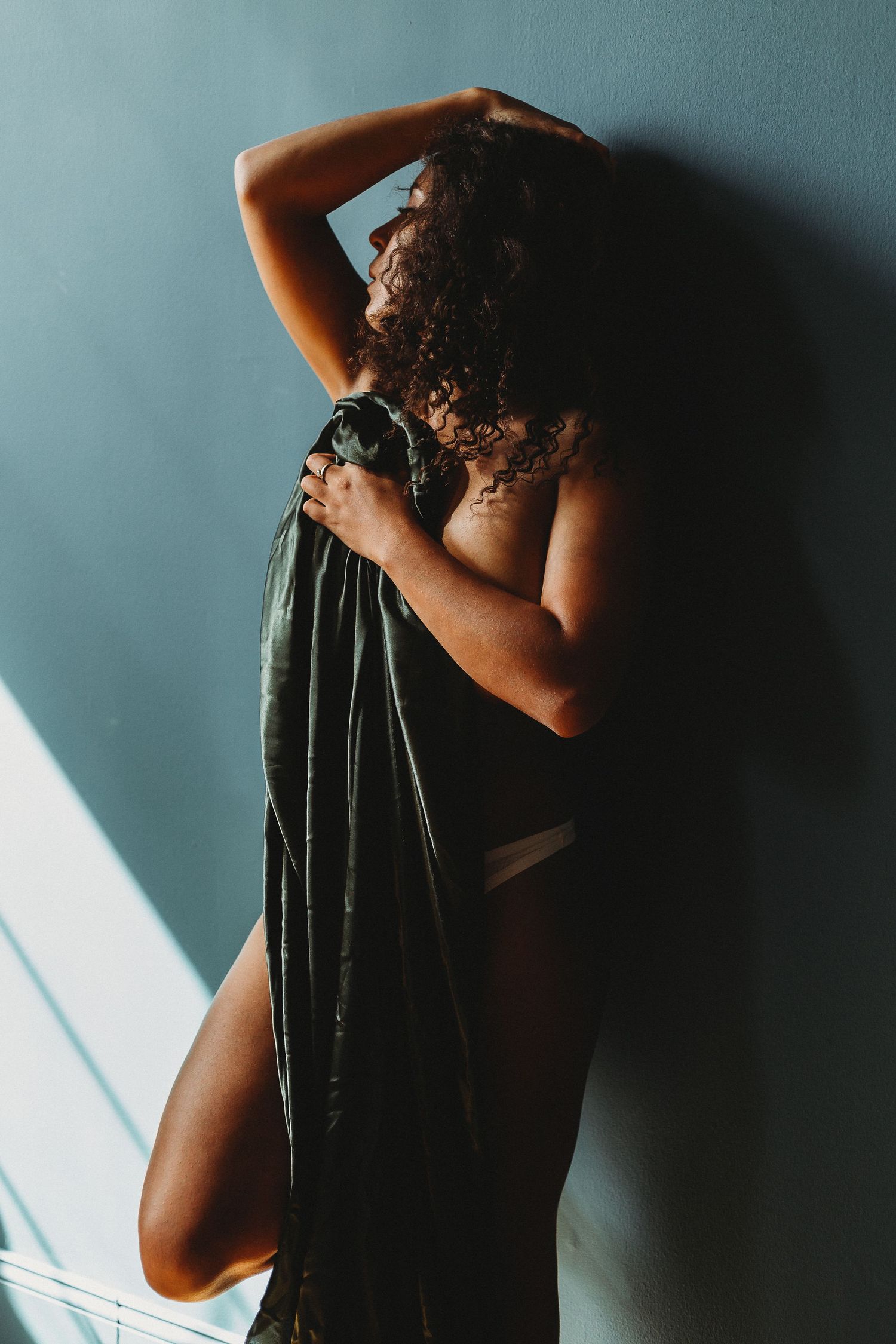 Silhouette portrait with flowing fabric against blue wall in dramatic lighting.