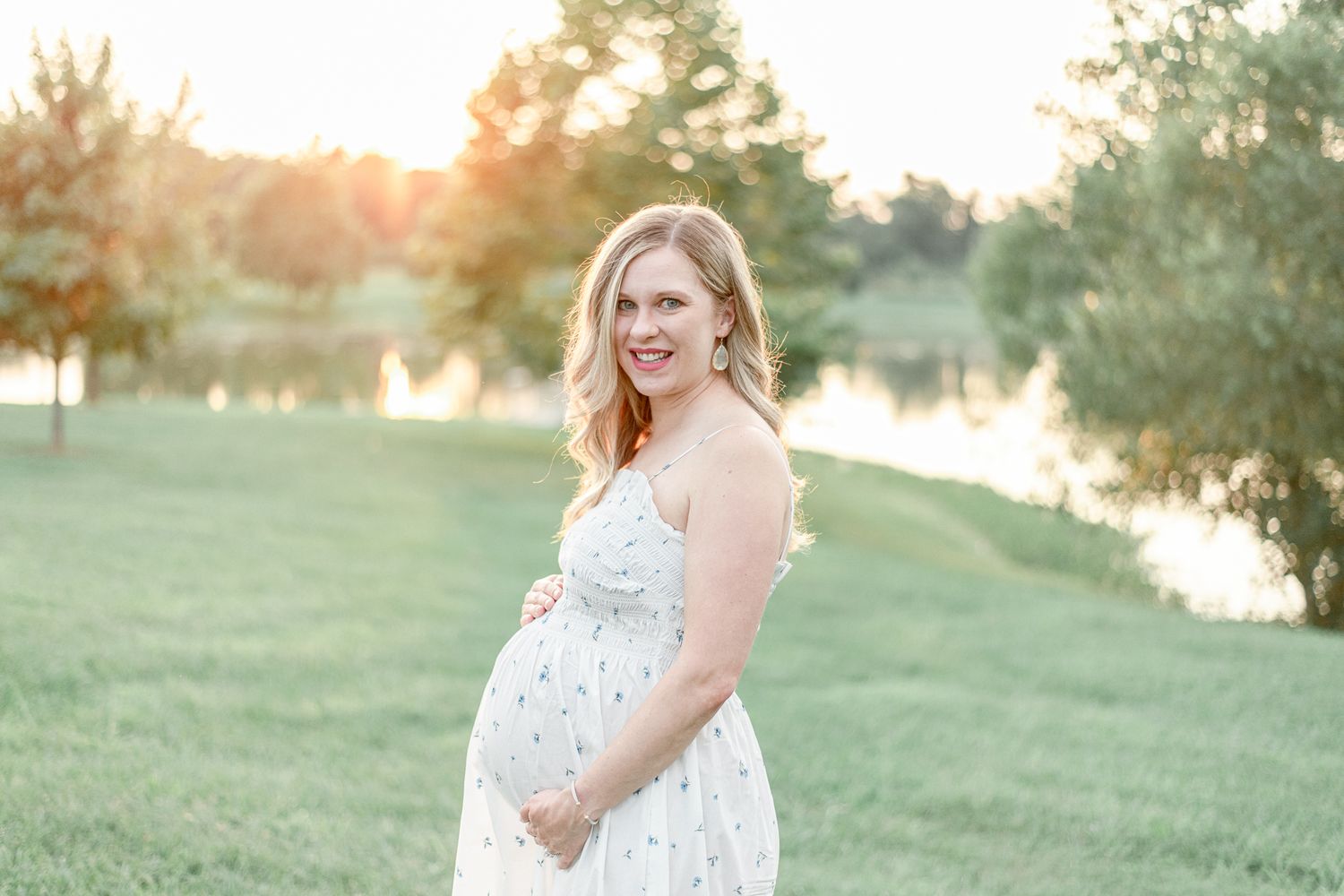 Maternity image of a young woman with a pond and golden sunset behind her