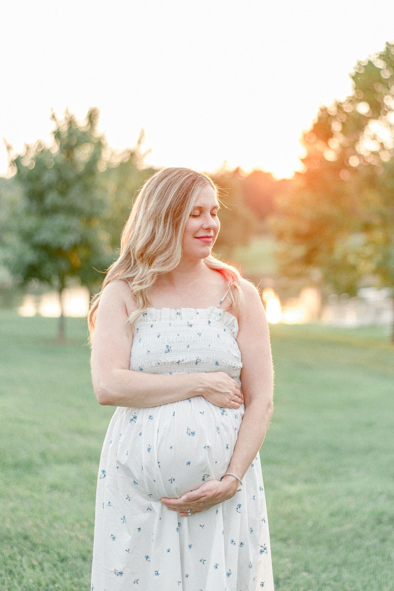 Pregnant woman cradles her baby with her eyes closed at sunset