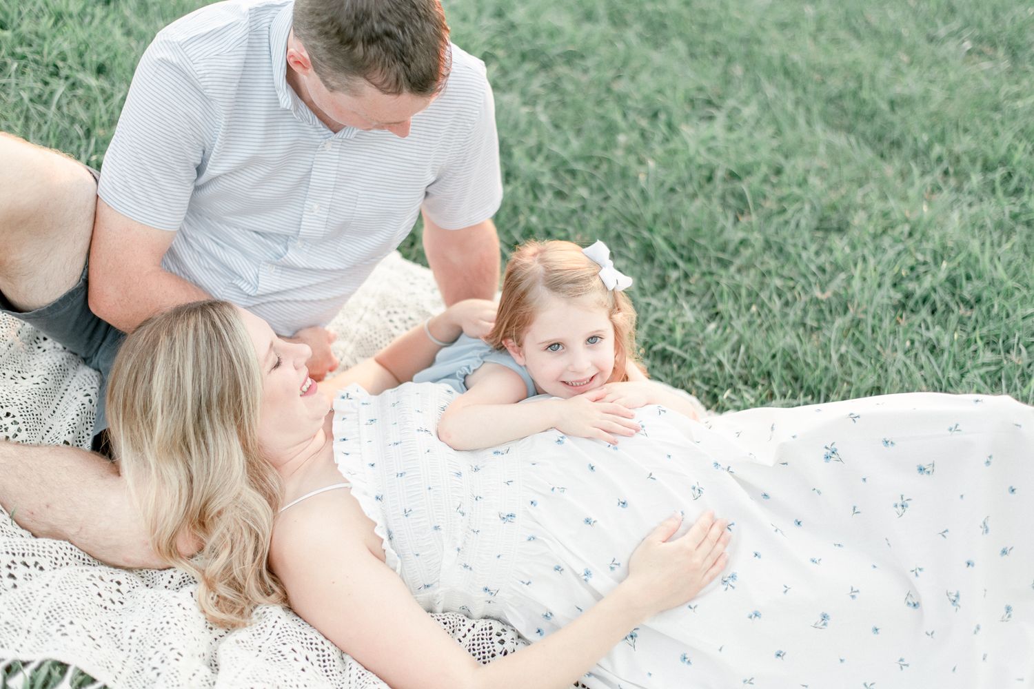 Little girl lays her head on her mother's pregnant stomach and mother's head in her husbands lap