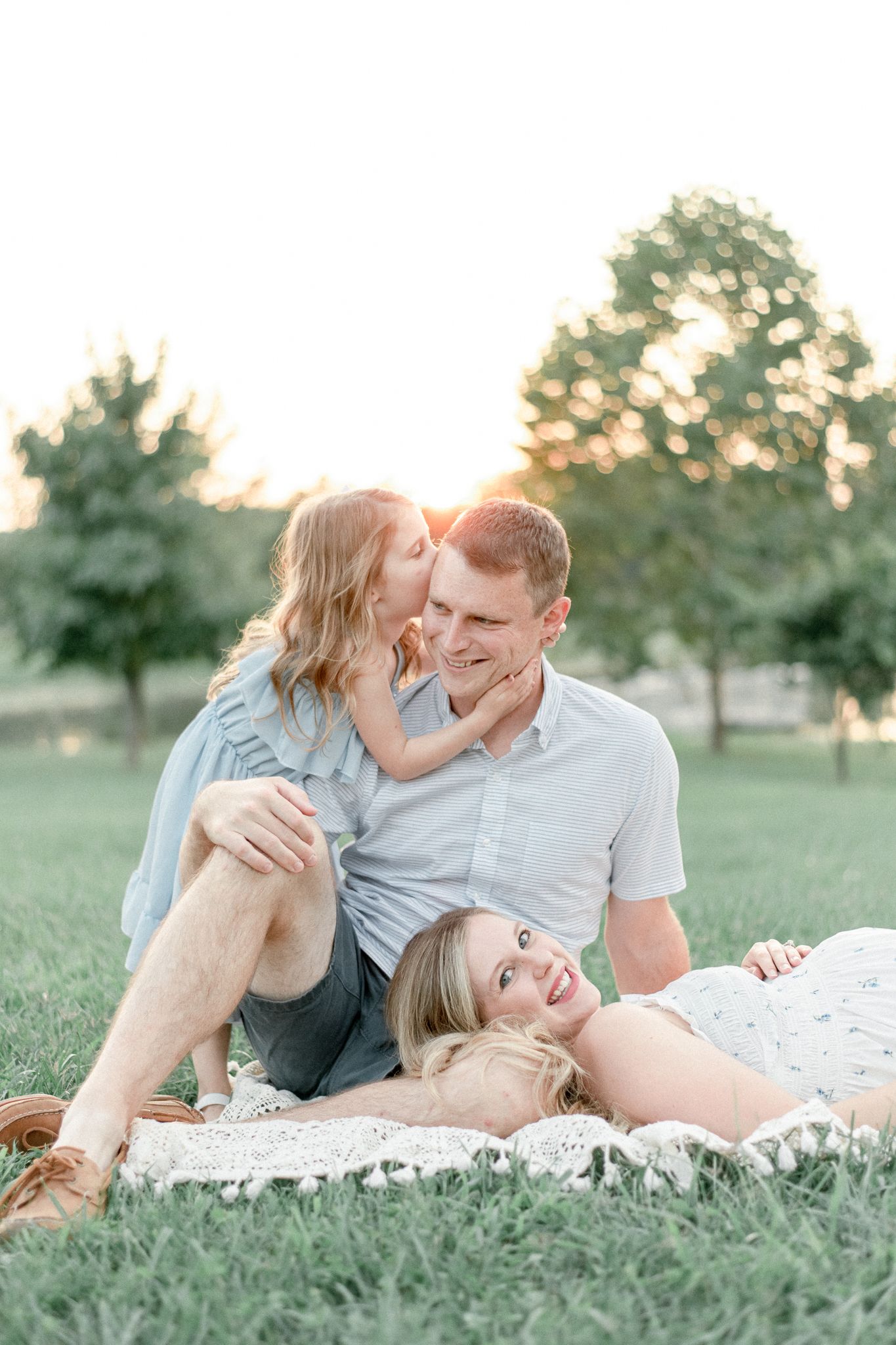 Little girl kisses dad on his cheek, his wife lays her head in his lap
