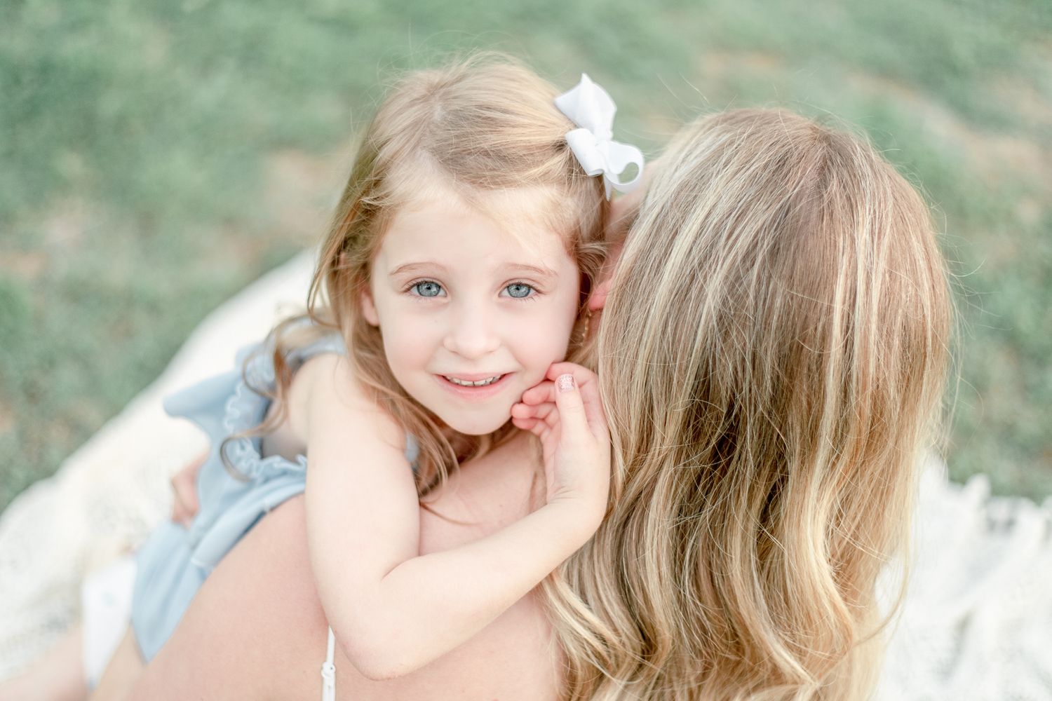 Little girl smiles up as she hugs her mother and rests her head on her shoulder