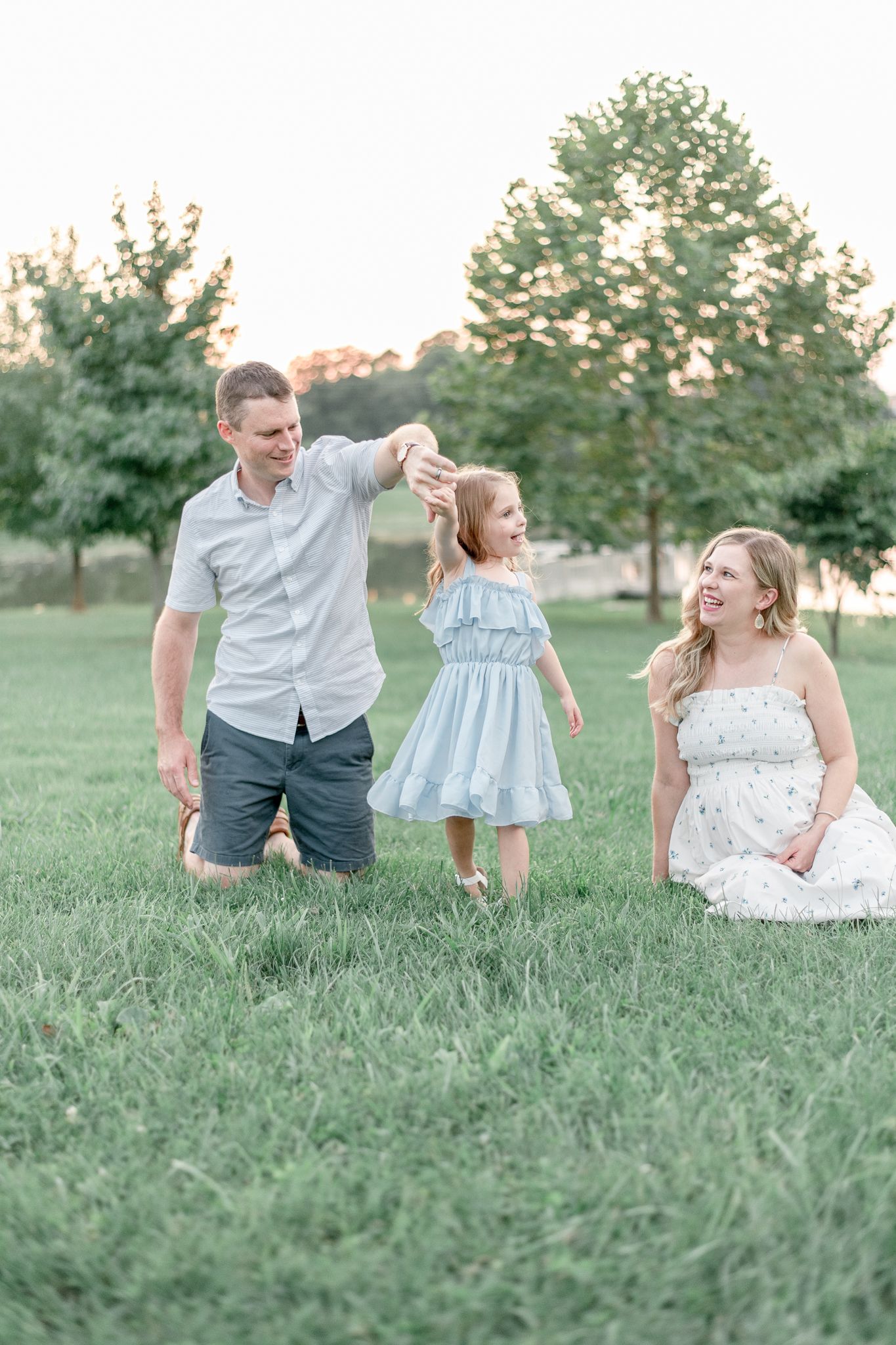 Father twirls little girl at sunset as the mother watches adoringly