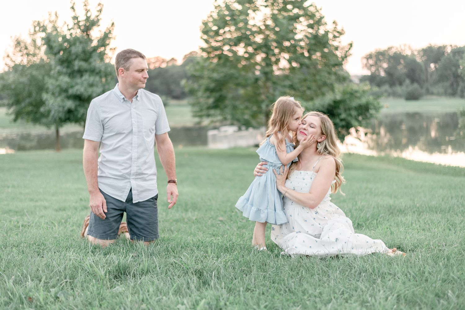 Little girl kisses pregnant mother on the cheek as father watches them adoringly