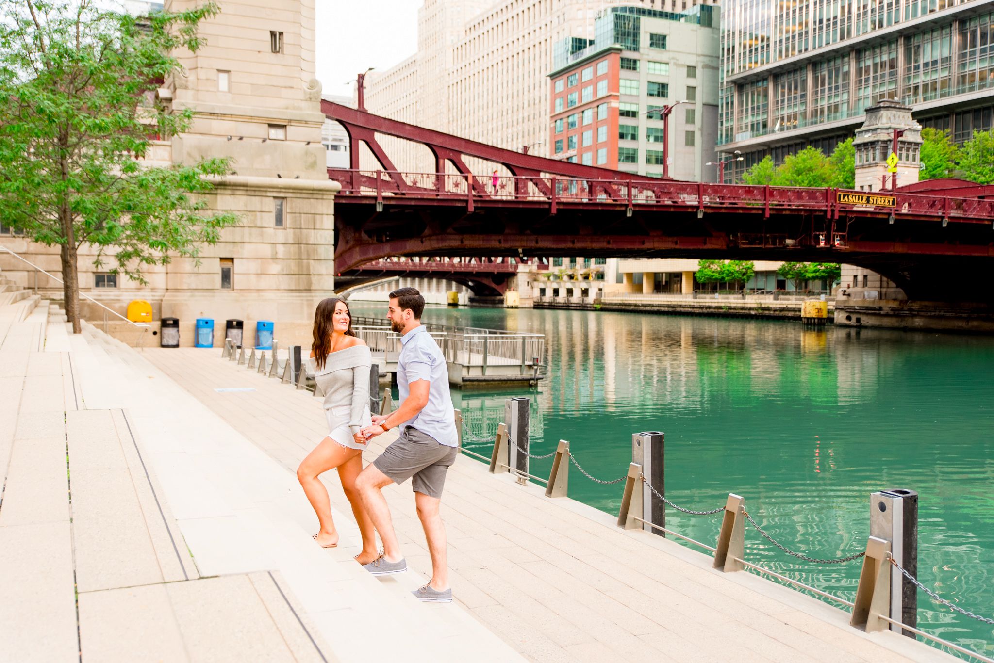 woman leading man up the steps at Chicago Riverwalk for engagement pictures in front of LaSalle Street Bridge