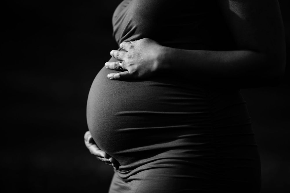Dramatic black and white side profile of pregnant belly with hands.