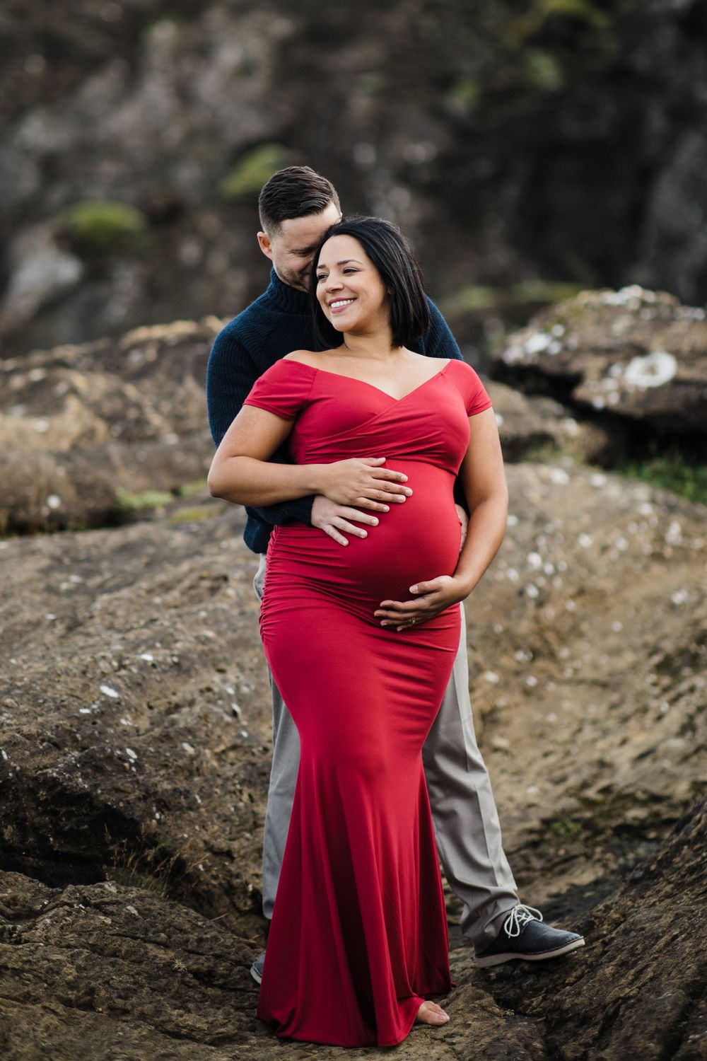 Maternity portrait of couple embracing by rocky outcrop.