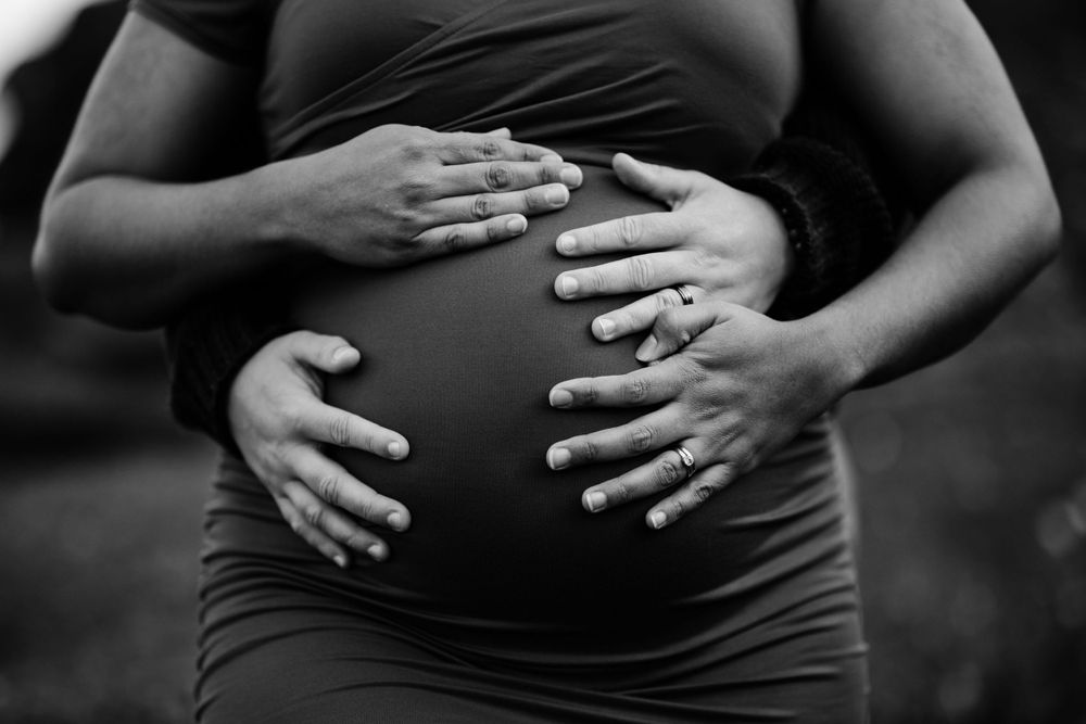 Black and white close-up of hands tenderly placed on pregnant belly.