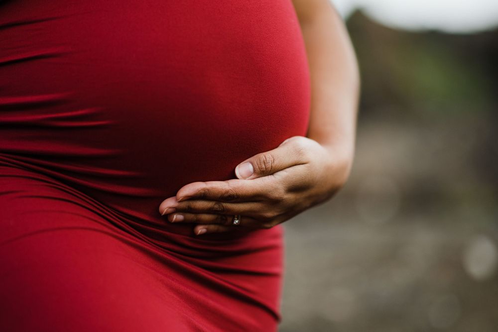 Close-up of hands cradling pregnant belly in red dress.