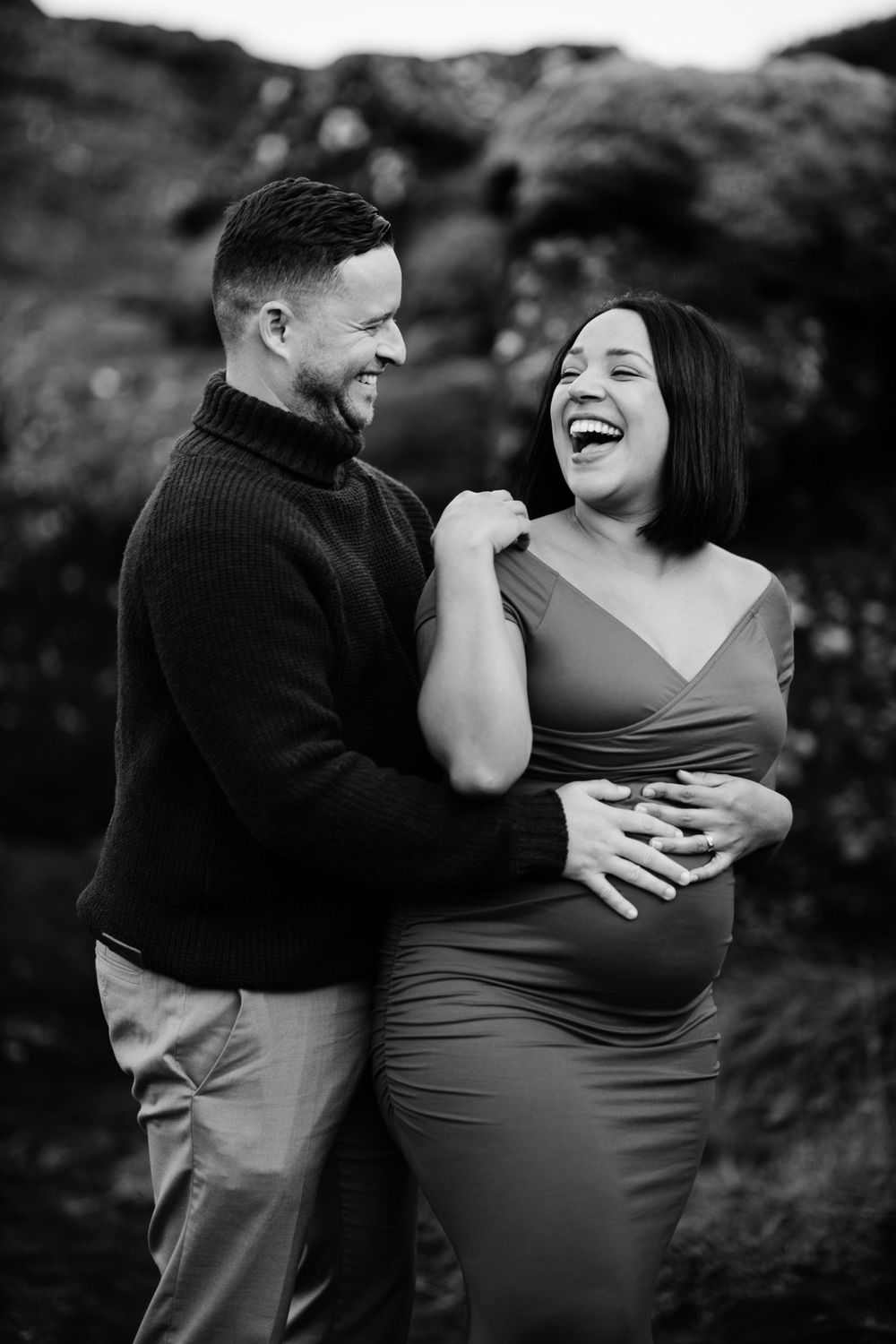 Joyful couple sharing a candid laughing moment during maternity photoshoot.