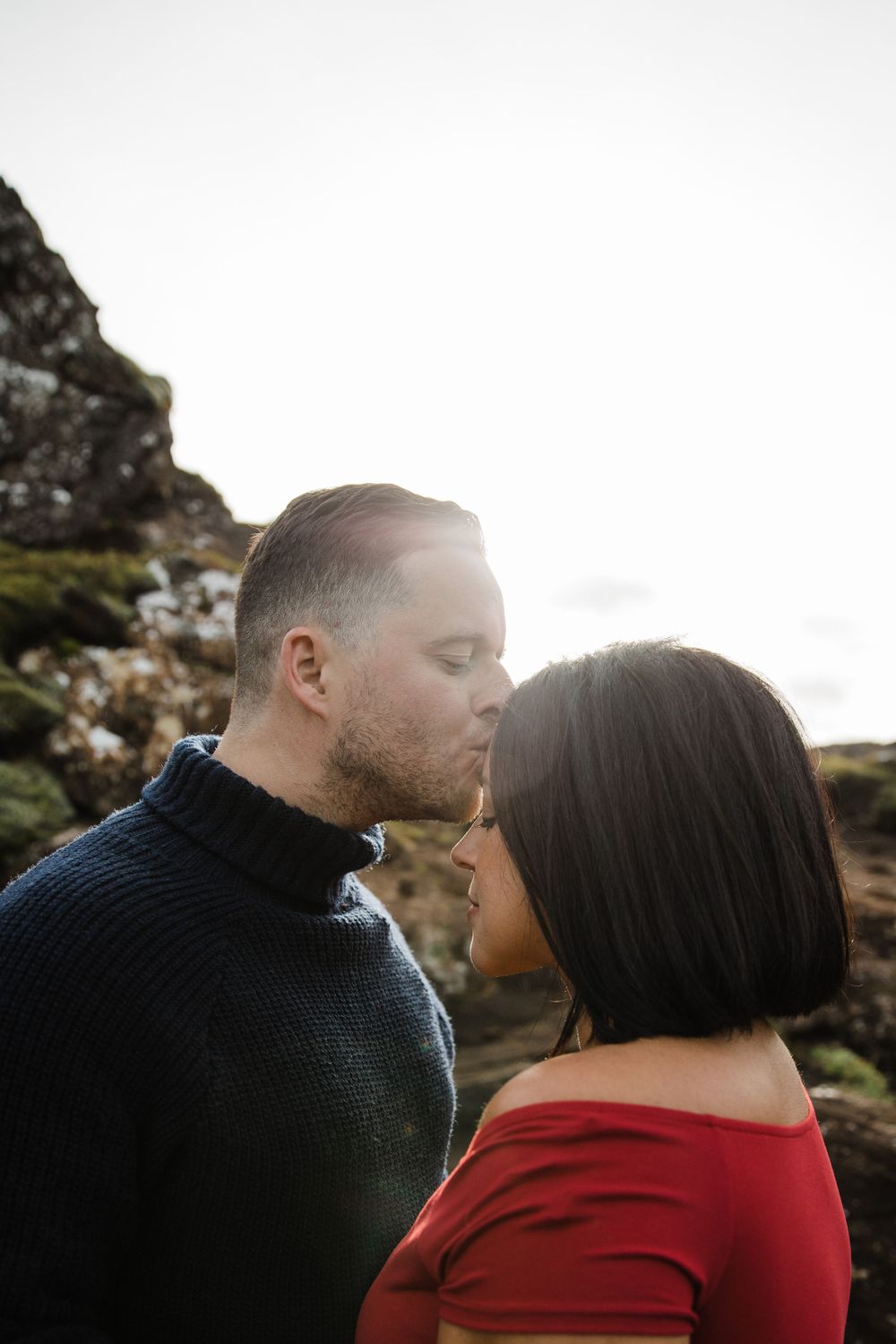 Intimate moment between couple against cloudy natural backdrop.