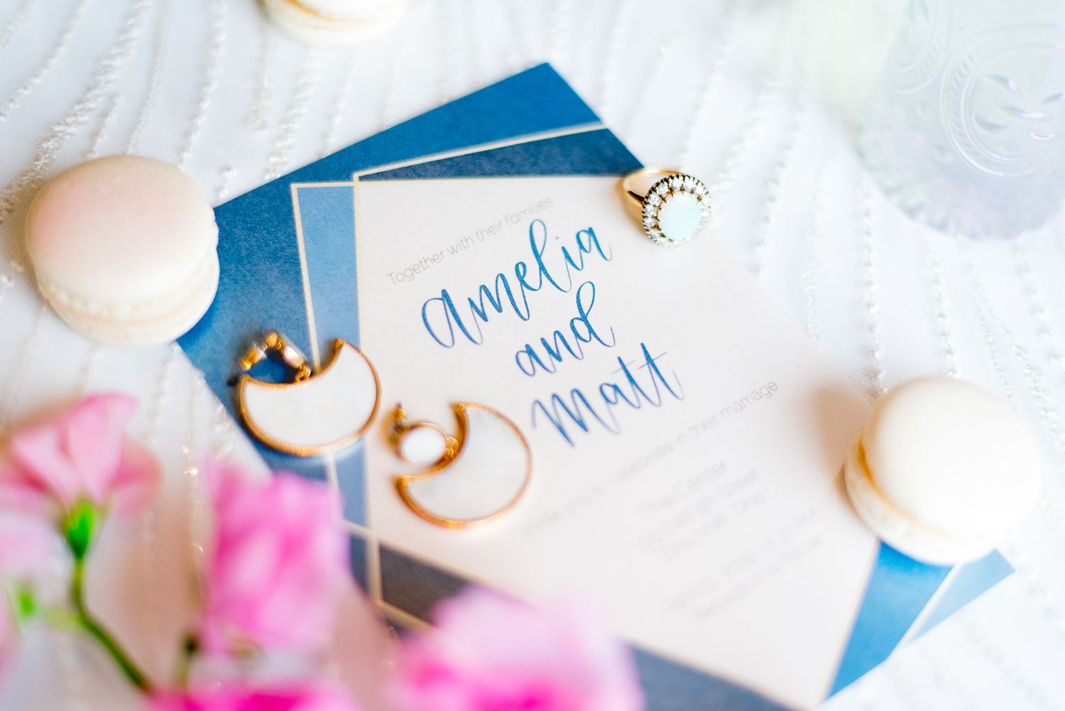 blue and white wedding invitation decorated with earrings, macarons, opal ring, wedding dress, and sweet pea flower