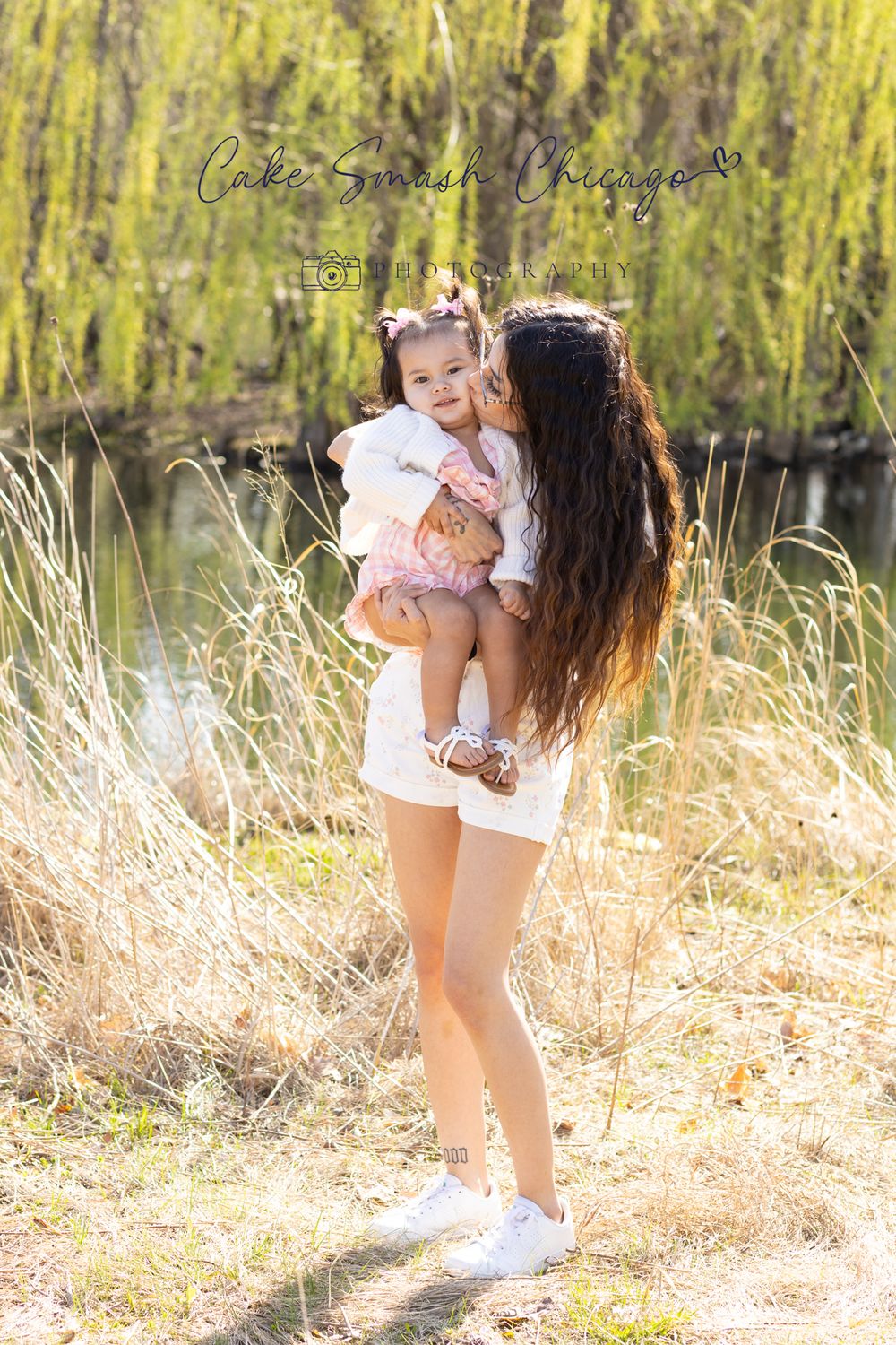 A tender embrace captured in golden sunlight with tall grass and a willow tree in the background.