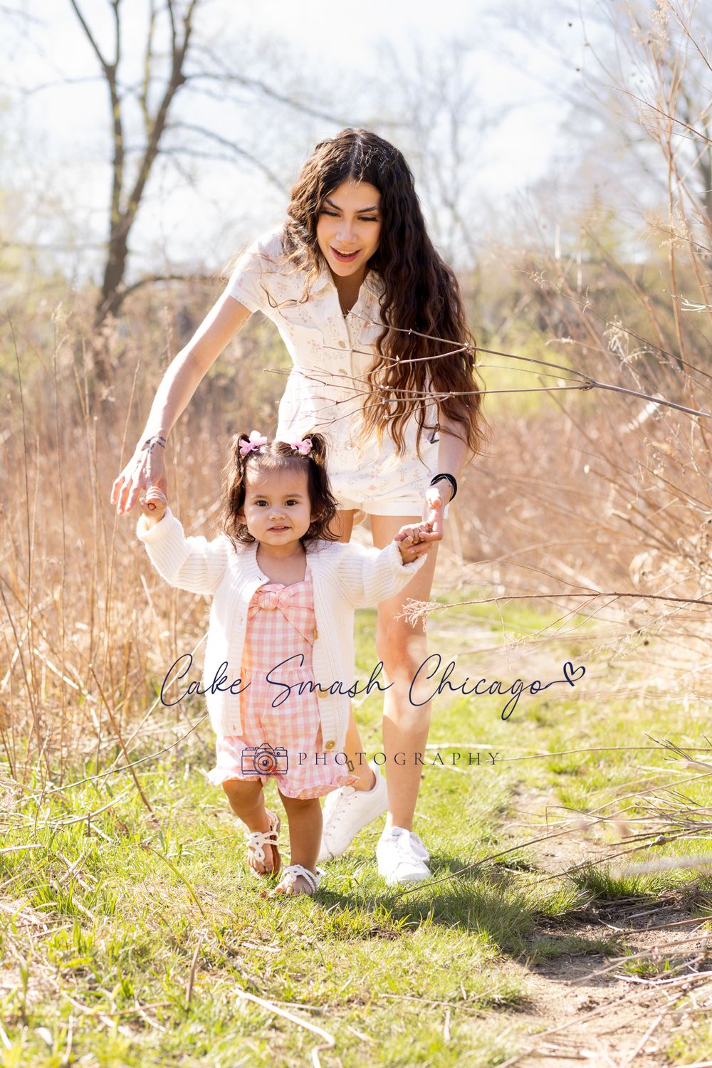 A parent and child walking hand in hand along a nature path surrounded by tall grass and trees.