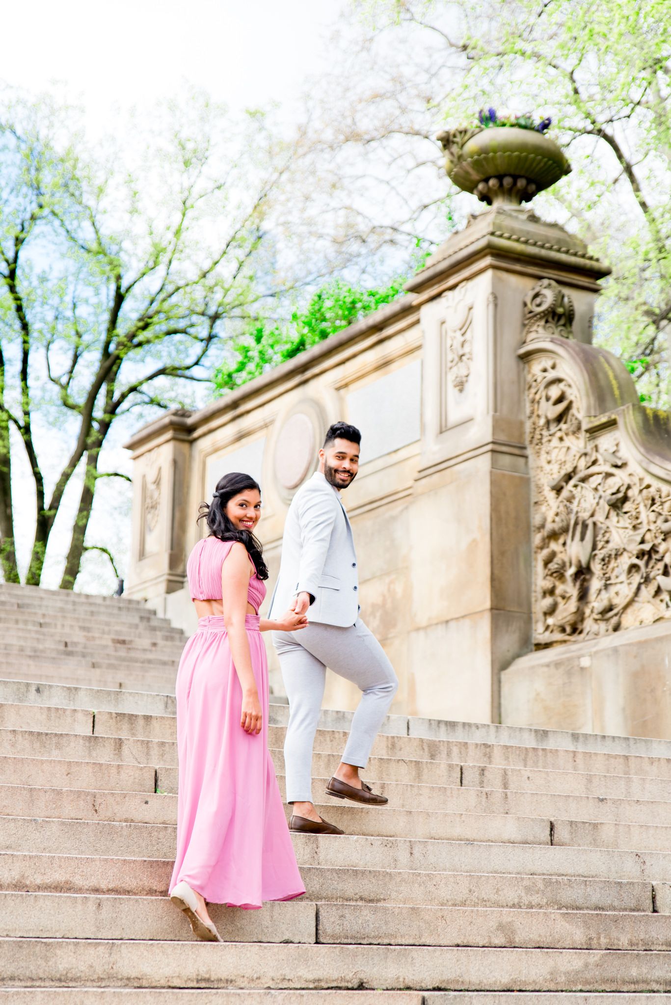 engaged couple holding hands walking up steps at Bethesda Terrace for Central Park spring engagement photos