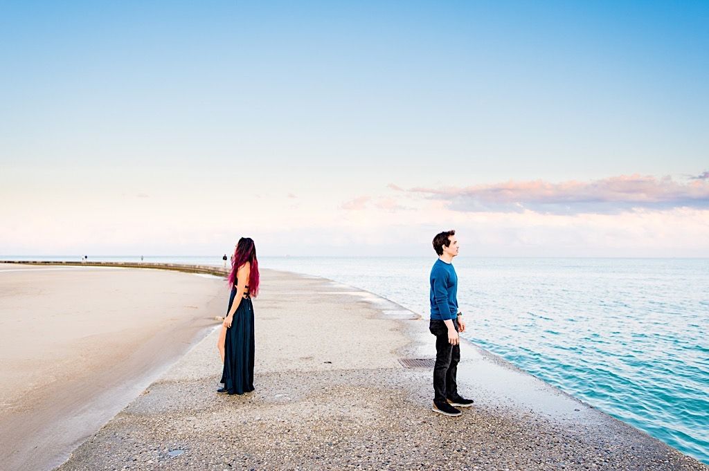 man and woman stand back to back far apart on North Avenue Beach at sunset