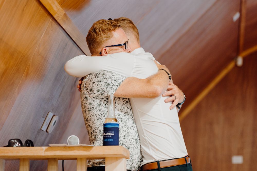 Two people share a warm embrace in a rustic wooden interior space.
