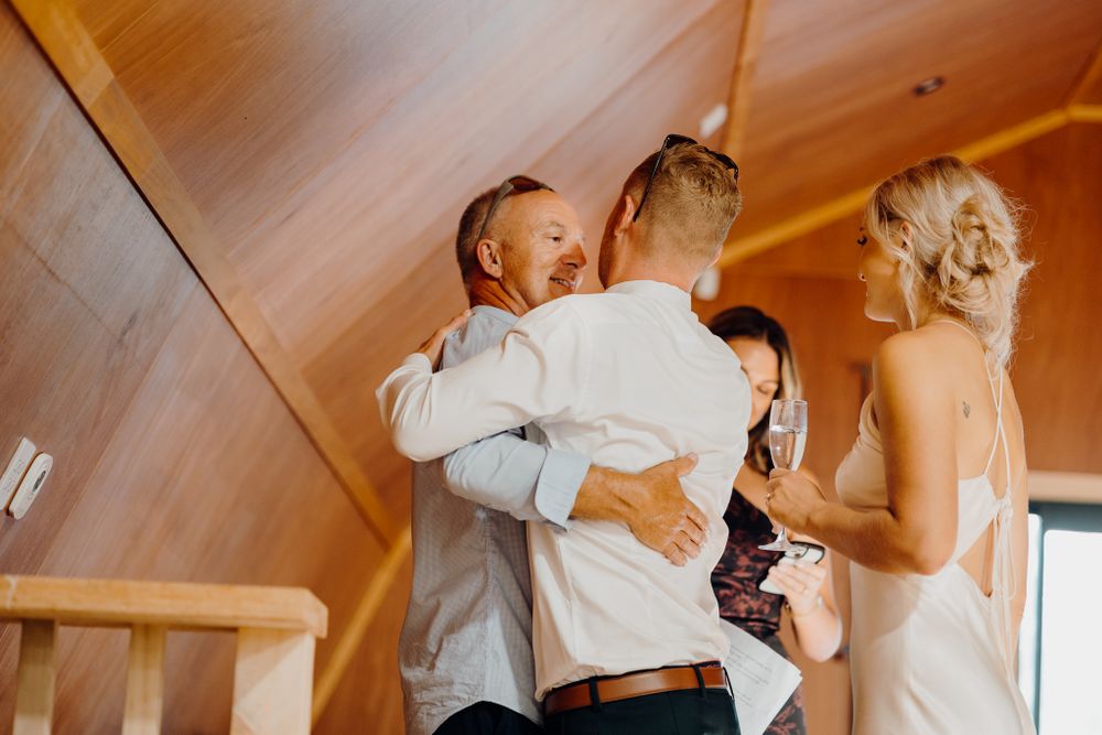 A tender emotional moment shared between three people embracing in a wooden room during a celebration.