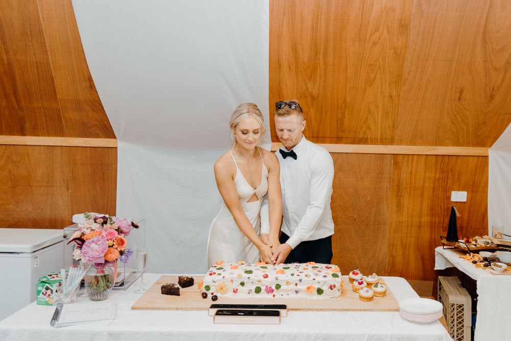 Couple cuts wedding desserts at modern reception with wood paneled walls.