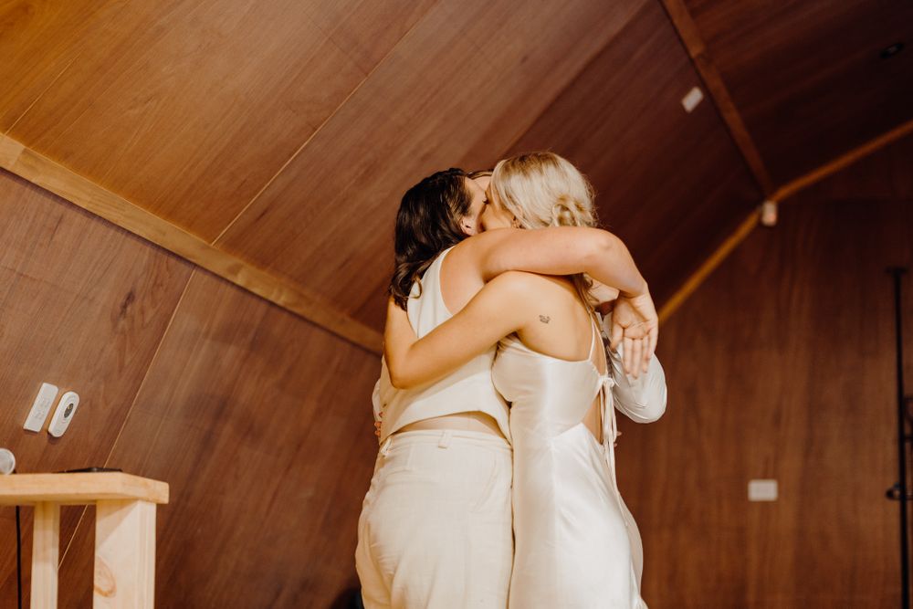 Two people in white dresses embrace emotionally during a celebration.