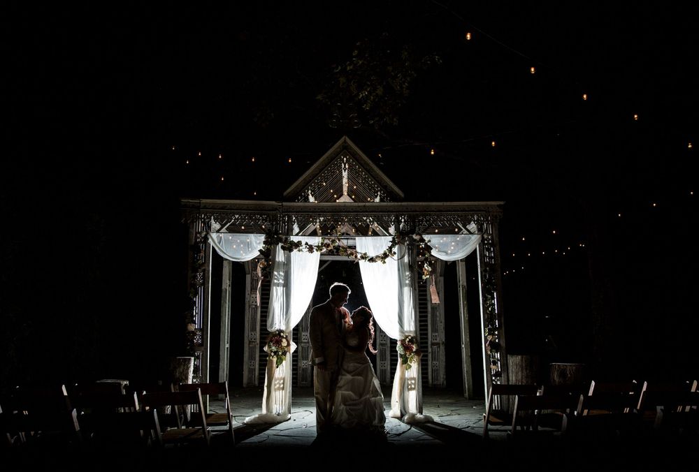 Dramatic nighttime wedding ceremony under illuminated gazebo with silhouetted figures.