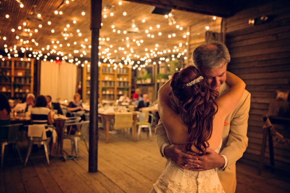 Romantic couple embracing under warm string lights at rustic reception venue.