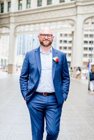 man in navy suit and glasses standing under Wrigley Building Chicago