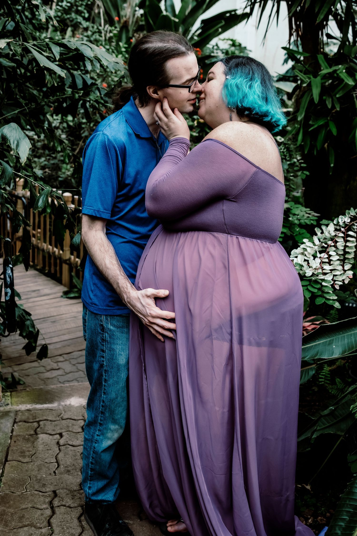 A romantic couple embracing in a greenhouse, wearing blue and purple clothing.