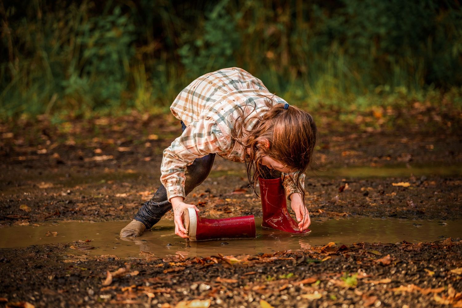 Girl using her gumboot as a bucket in a muddy puddle