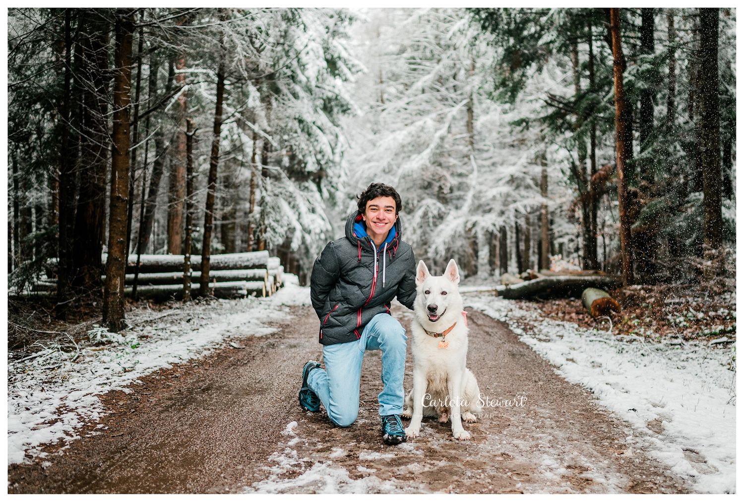 Teenager posing next to his white dog in the snow woods in Lower Austria