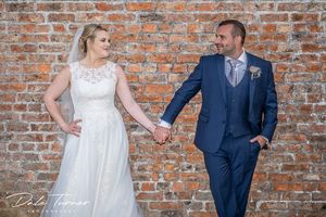 Bride and groom looking at each other, holding hands and leaning against a red brick wall.