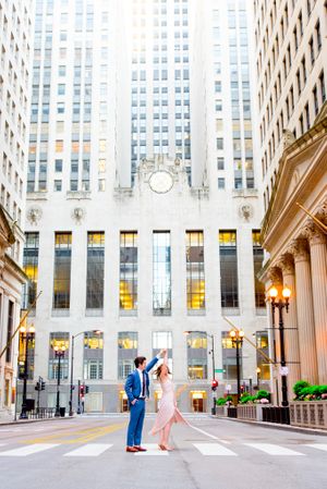 man and woman spin around in the empty street in front of Chicago Board of Trade for engagement pictures