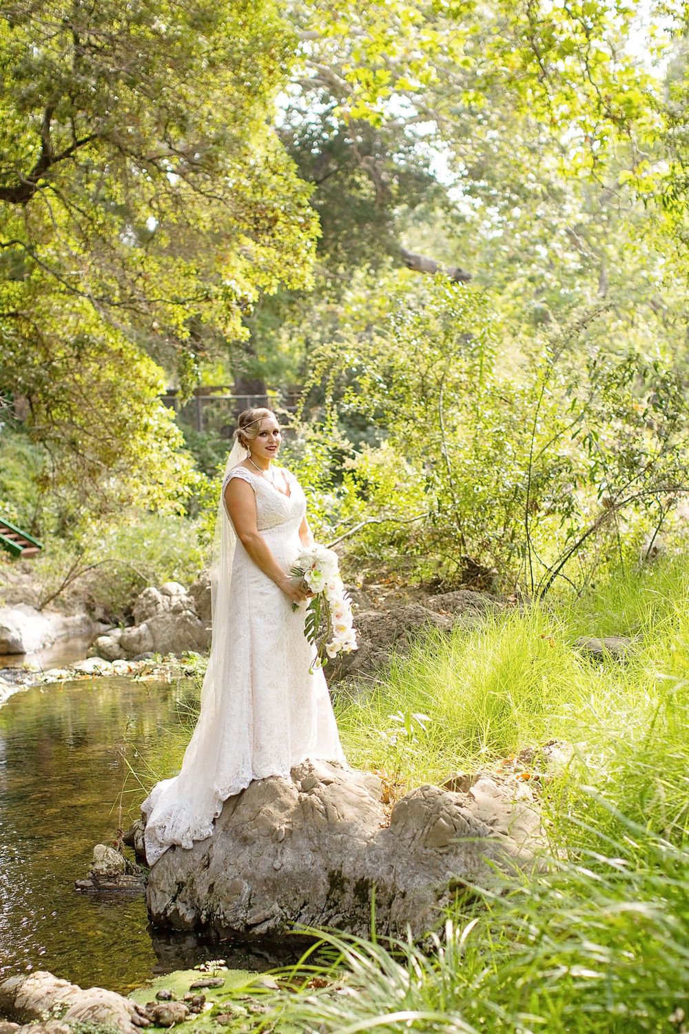 Bride standing on rock in creek near Monday Club in San Luis Obispo