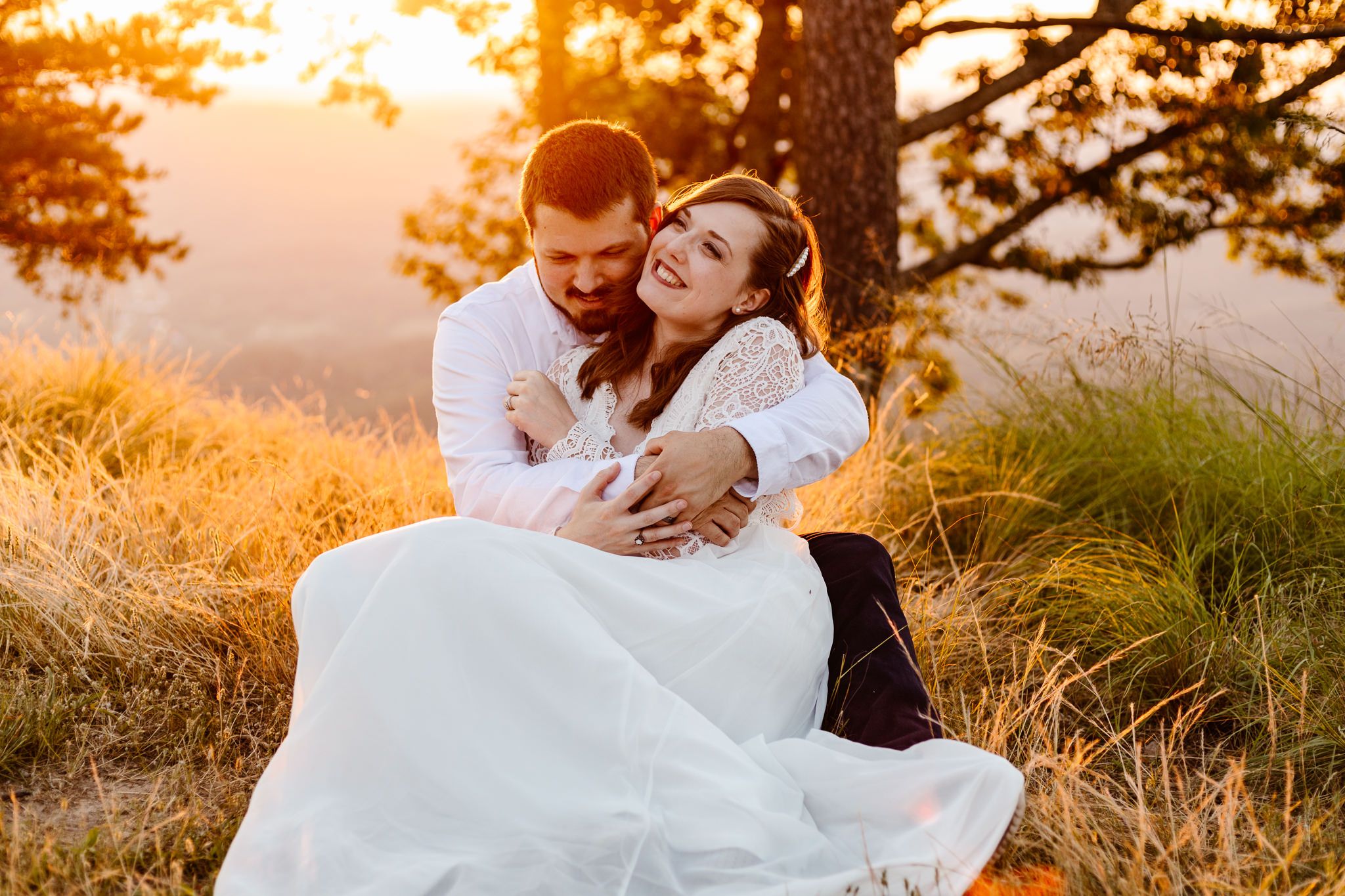 Husband squeezes his wife to make her laugh while eloping at sunset.
