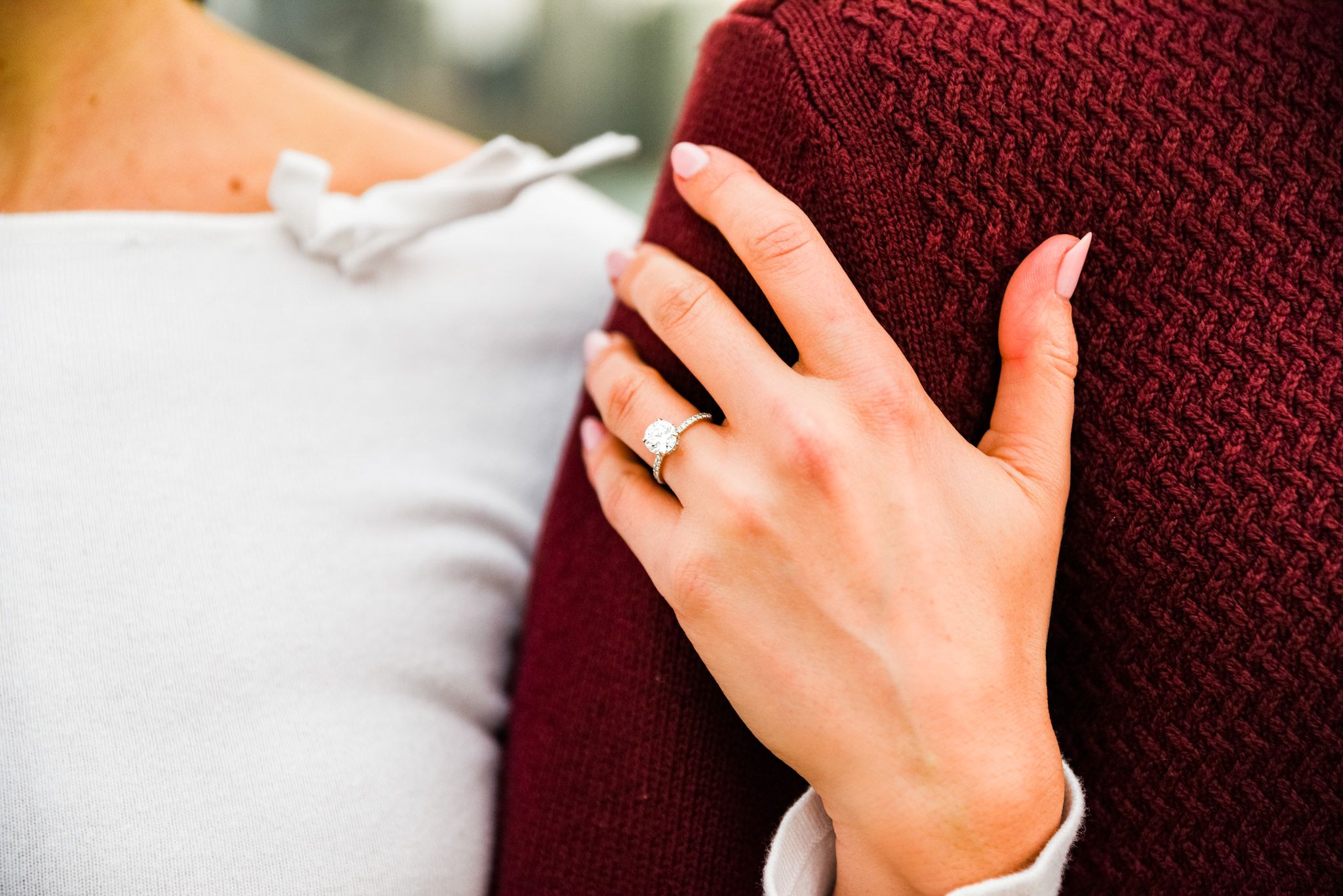 woman's hand with engagement ring wrapped around man's arm in red sweater