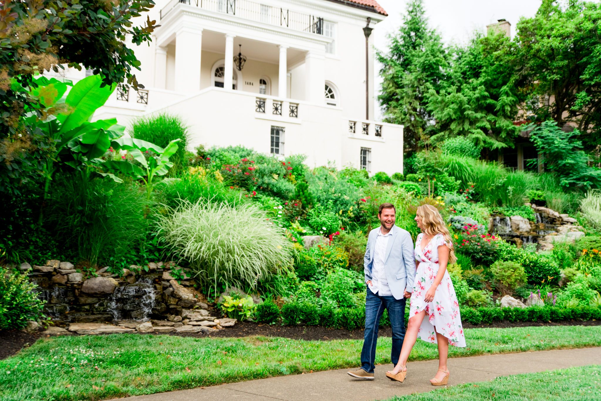 engaged couples in floral dress and light blue suit jacket and jeans walking in rainy Louisville white mansion