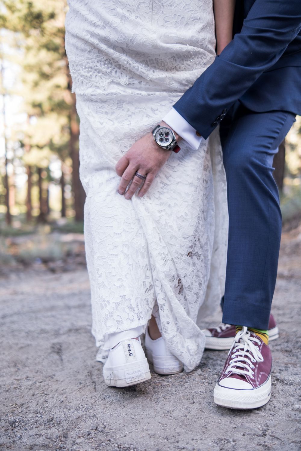 A couple in wedding attire shows contrast between formal dress and casual sneakers in an outdoor forest setting.