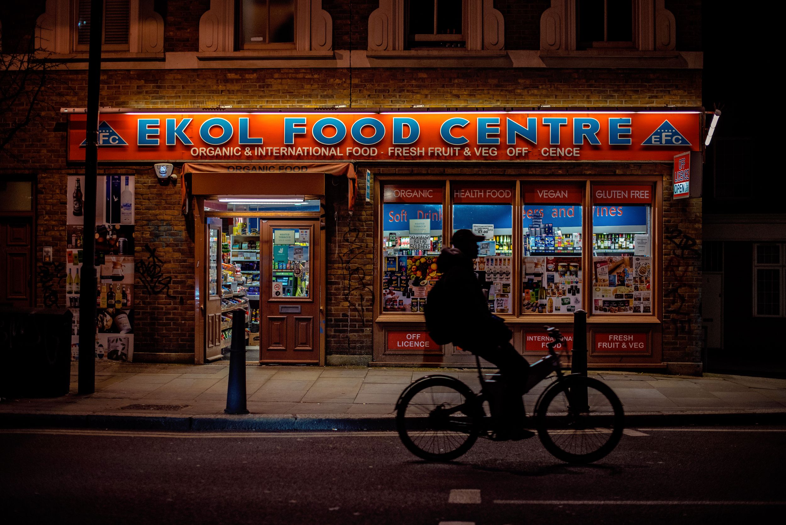 Silhouette of a man riding his bike past lit food centre in London's Shoreditch neighborhood