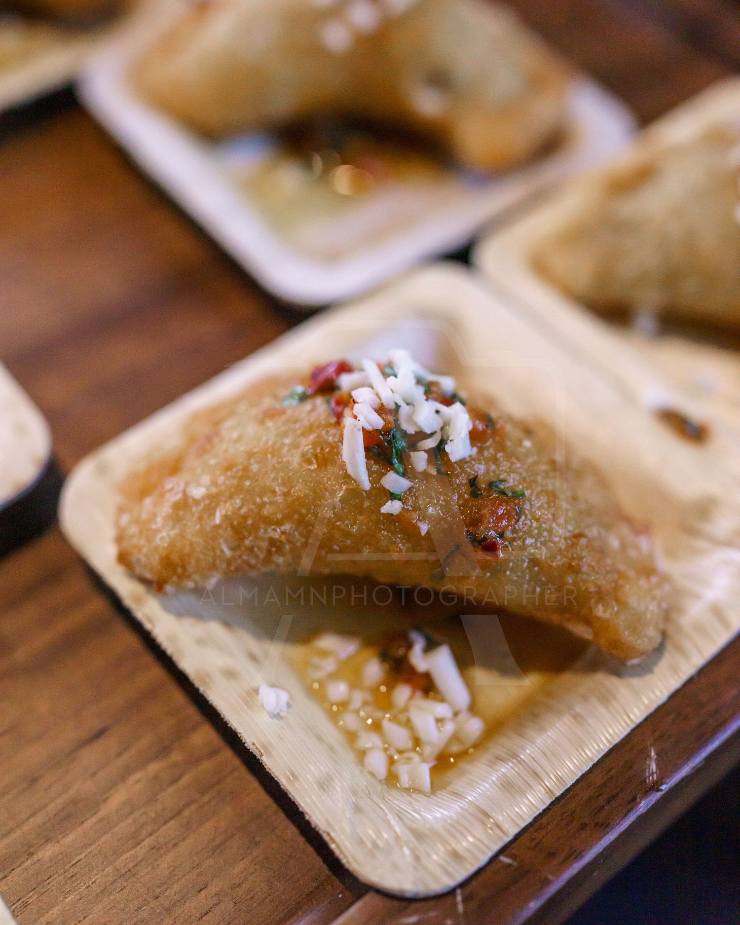 Golden fried empanada topped with shredded cheese on a wooden serving plate.