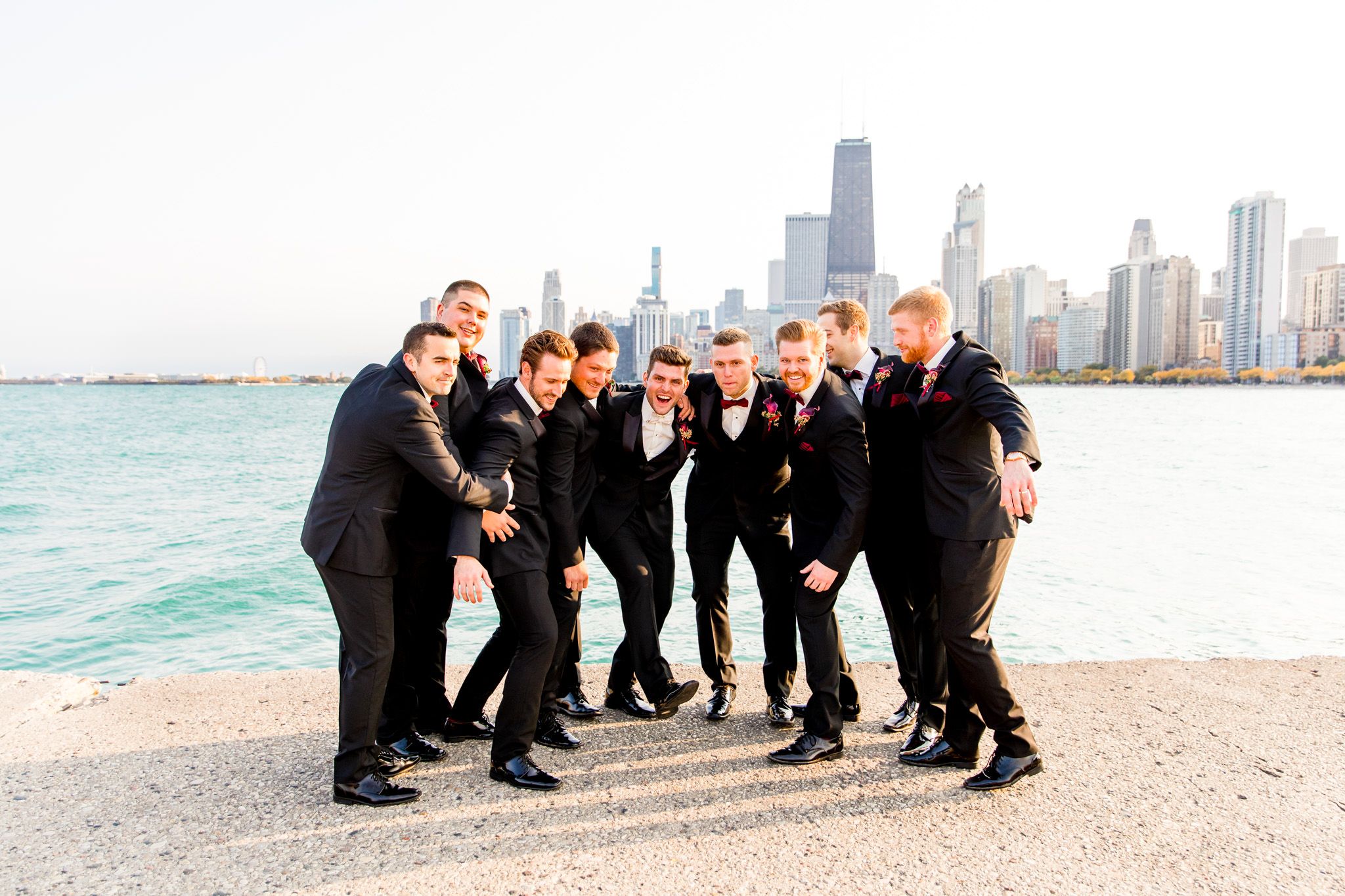 groomsmen huddle around groom in front of lake michigan and chicago buildings