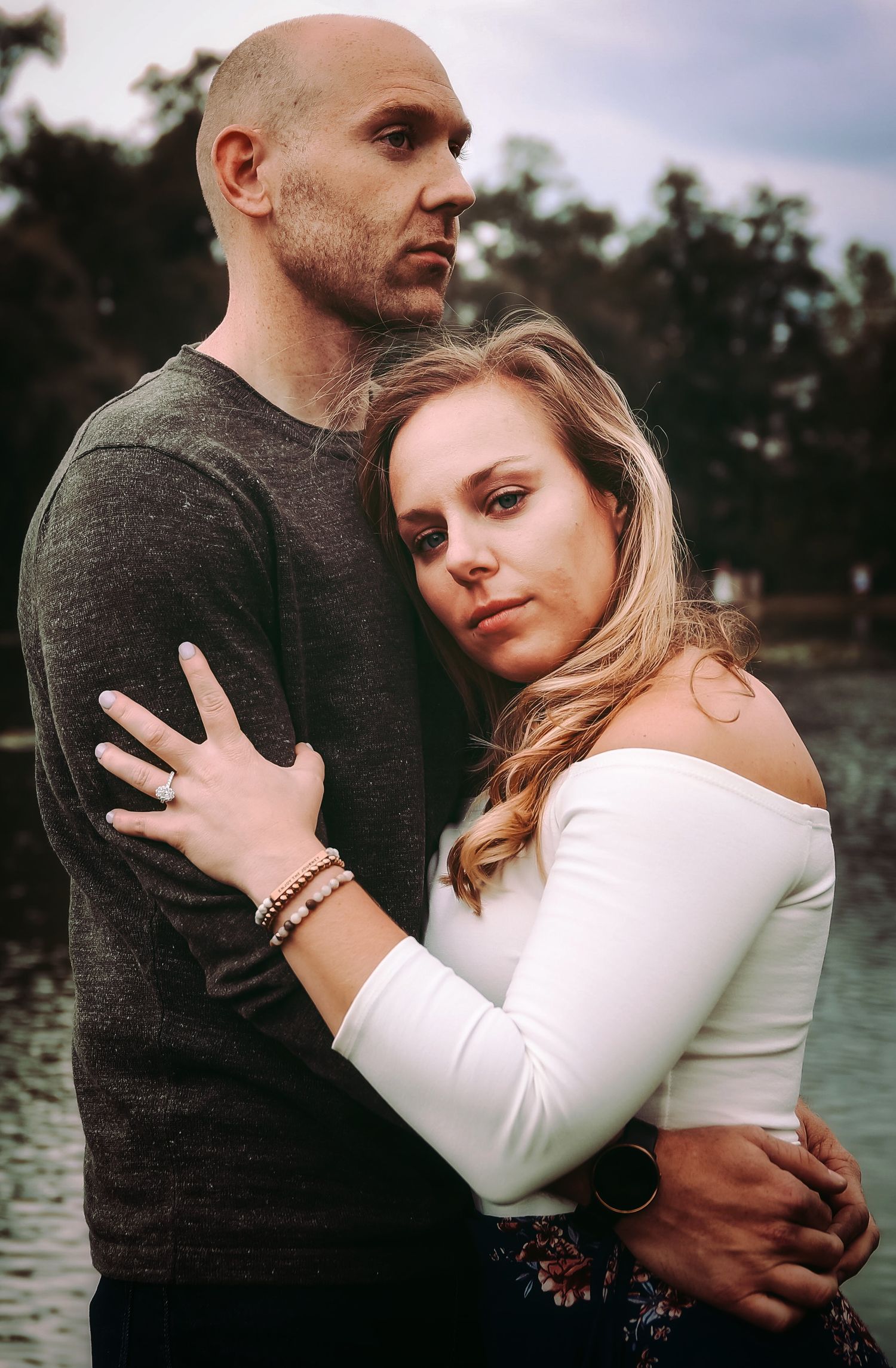 An intimate portrait of a couple embracing outdoors near water.