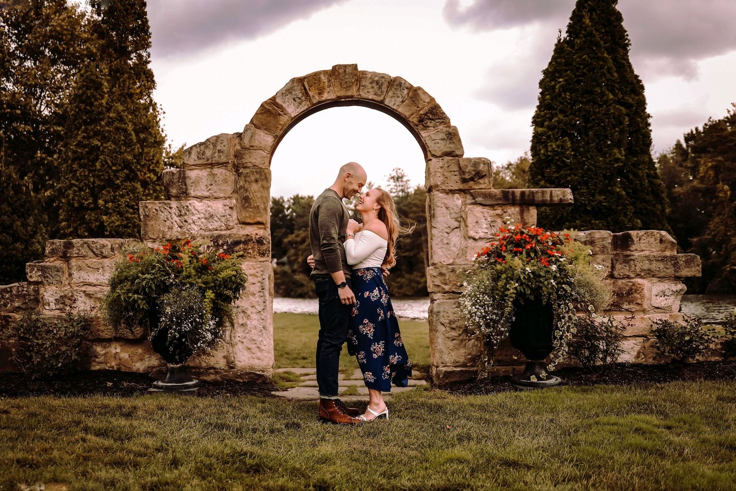 A couple sharing a tender moment under a rustic stone archway with blooming flowers.