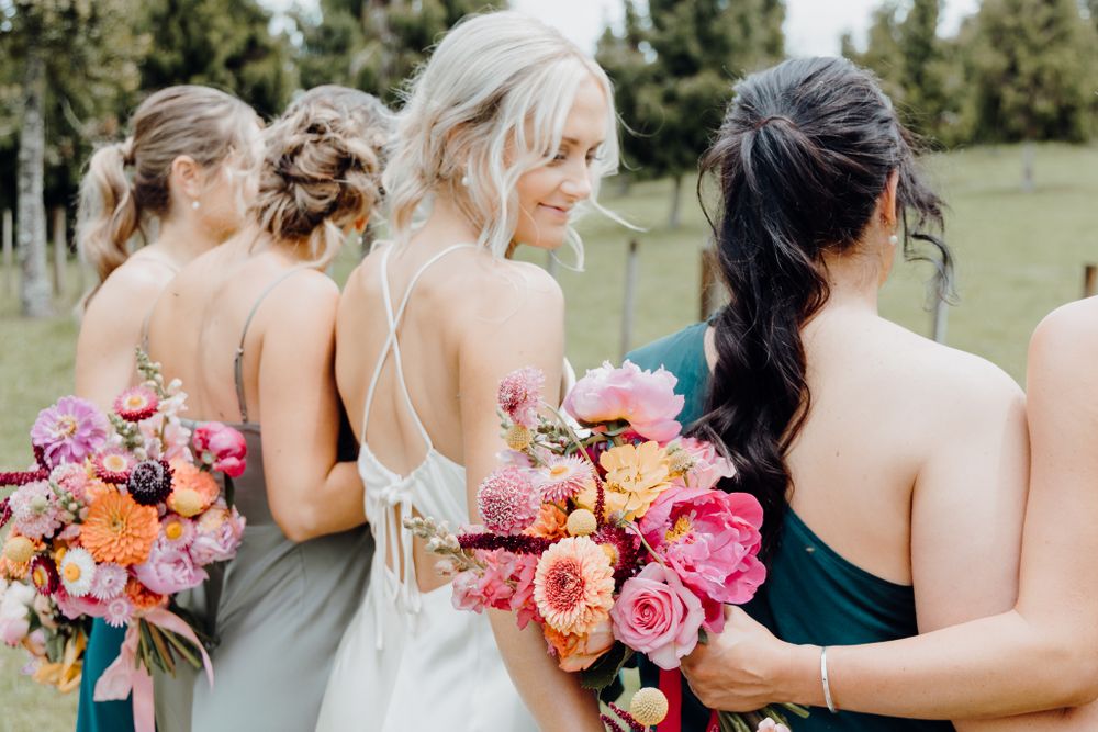 Close up of bridal party from behind holding pink and coral bouquets.