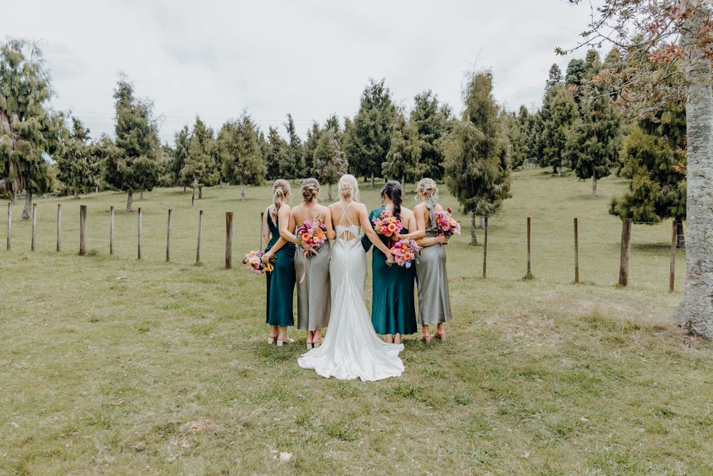 Bridal party in teal and grey dresses stands together on grassy field.