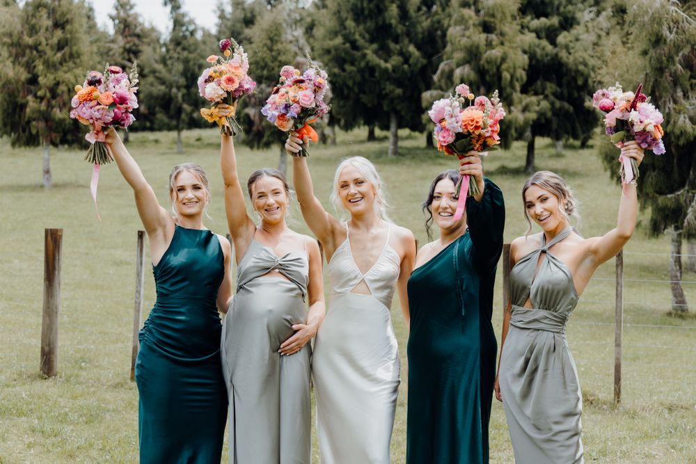 Bridesmaids in teal and grey dresses raise colorful bouquets in celebration.