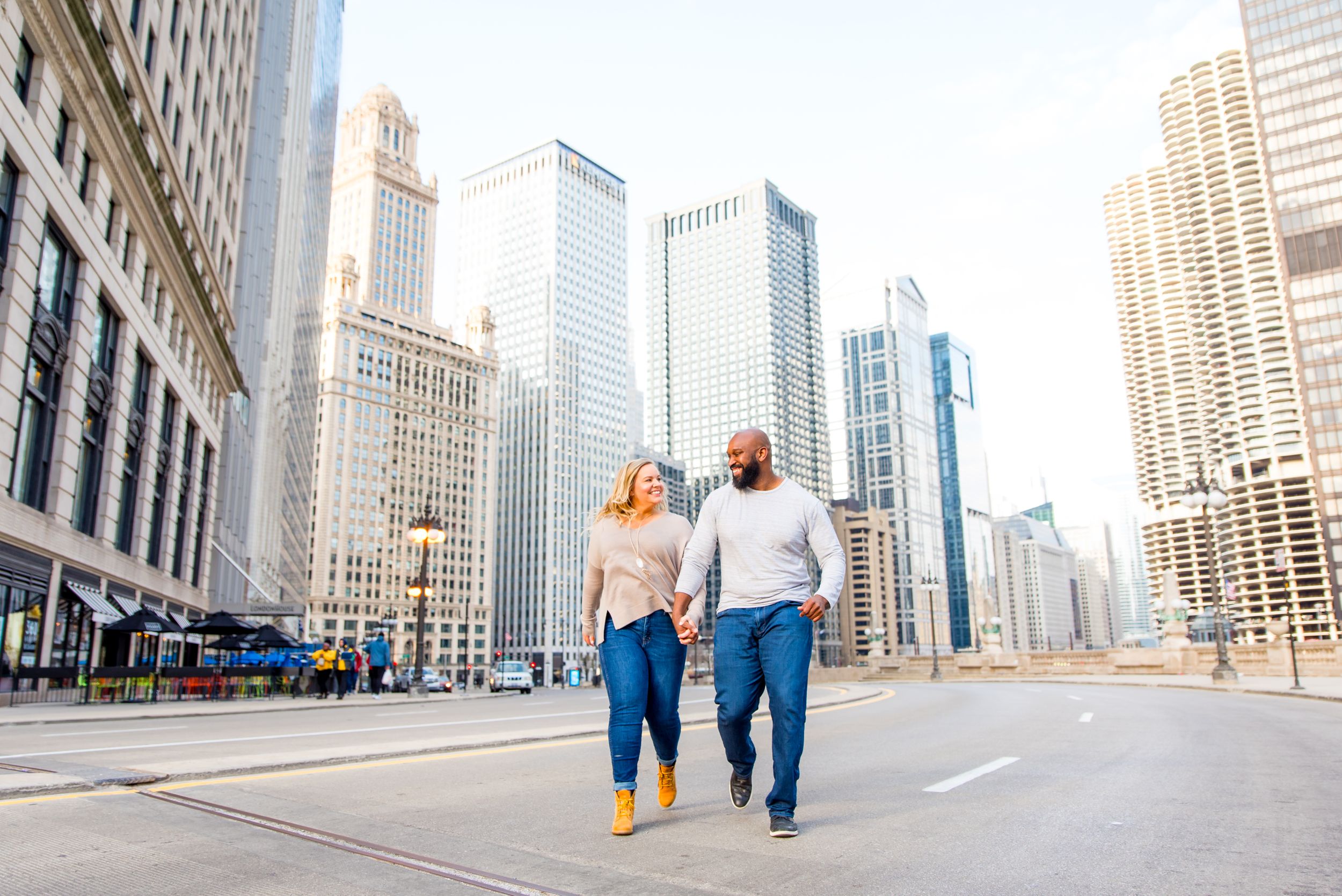 man and woman holding hands smiling running through Michigan Ave for Chicago engagement photos
