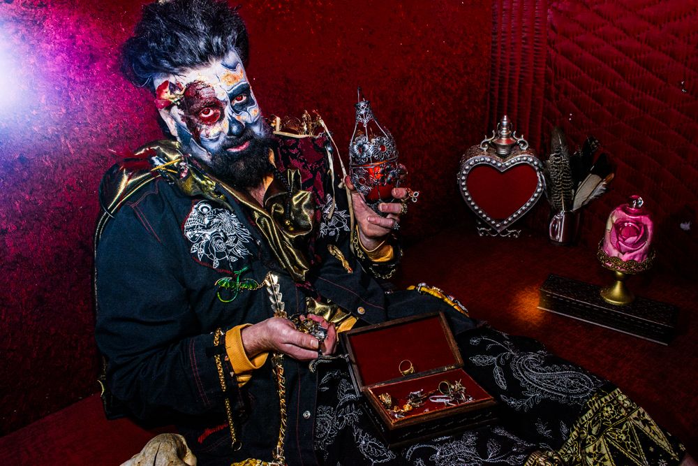 Gothic themed scene with skull makeup and antique decorative objects against red lighting.